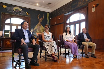 Cuatro personas, dos hombres y dos mujeres, sentadas en sillas de cuero oscuro en una sala con paredes de madera y un mural colorido