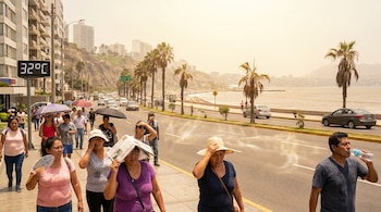 Calle en Lima con personas protegiéndose del sol intenso; sombrillas y periódicos. Un cartel digital muestra 32°C. Edificios, carretera y mar visible al fondo.