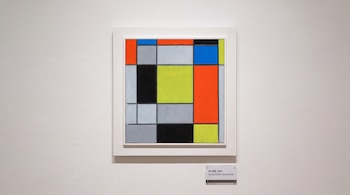 Pintura con cuadrados y rectángulos de colores en marco blanco, colgada en una pared junto a una cartela con texto.