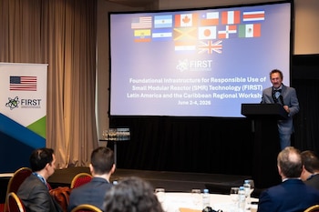 Hombre en podio en un seminario. Pantalla grande con banderas, logo FIRST y título "SMR Technology Latin America and the Caribbean Regional Workshop". Audiencia