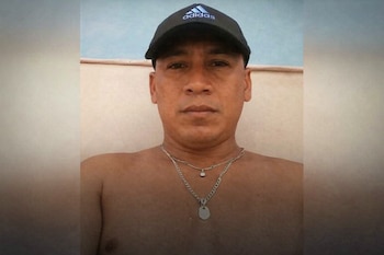 Primer plano de un hombre con gorra negra Adidas, dos cadenas plateadas en el cuello y torso descubierto. El fondo es de color claro.