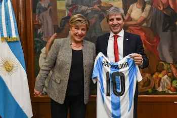Mujer y hombre sonriendo. Hombre sostiene camiseta de fútbol blanca y celeste con número diez y el nombre Kristalina. Bandera argentina y mural al fondo