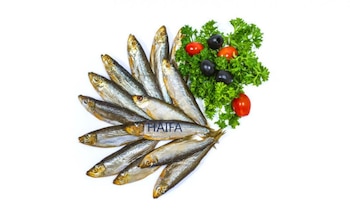 Pescados ahumados dispuestos en abanico sobre fondo blanco, acompañados de hojas de perejil, aceitunas negras y tomates pequeños