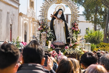 Una imagen religiosa de Santa Rosa de Lima decorada con flores es llevada en andas rodeada por una multitud en una calle