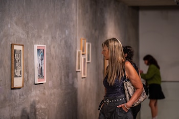 Vista lateral de una mujer con cabello rubio largo, top oscuro y shorts, mirando cuadros en una pared de hormigón en una galería