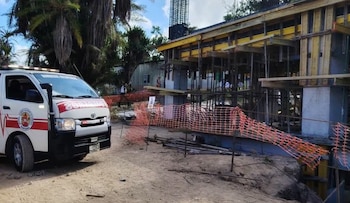 Camioneta blanca de bomberos estacionada junto a una obra en construcción rodeada por una malla naranja de protección