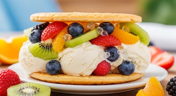 Primer plano de una galleta de hielo rellena de helado cremoso y una variedad de frutas frescas como fresas, arándanos, kiwi, frambuesas y gajos de naranja.