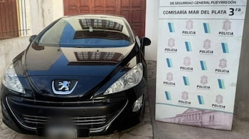 Un automóvil negro Peugeot estacionado frente a un portón de madera y junto a un cartel de la Policía de la Provincia de Buenos Aires