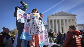 Dos jóvenes sostienen pancartas a favor de los derechos trans frente al edificio de la Corte Suprema, con otras personas y un cielo despejado de fondo