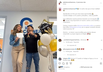 Isabel Acevedo e o marido estão sorrindo, ela com um envelope branco e ele com um molho de chaves, comemorando diante de balões e uma foto do escritório.