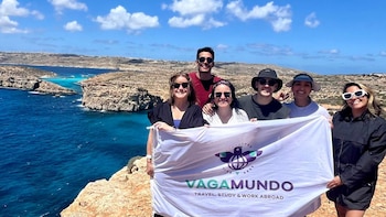 Seis personas posan en un acantilado con una bandera blanca con el texto Vagamundo frente al mar