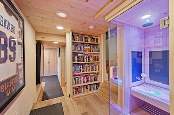 Pasillo interior con techo y suelo de madera, estantería con películas, sauna infrarroja con luz púrpura y camiseta deportiva enmarcada