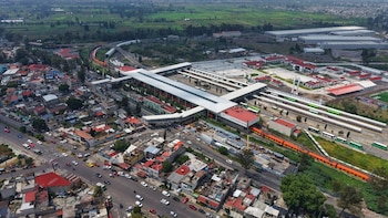 Vista aérea de una estación de transporte público con trenes, autobuses, vehículos en calles circundantes y zonas en construcción