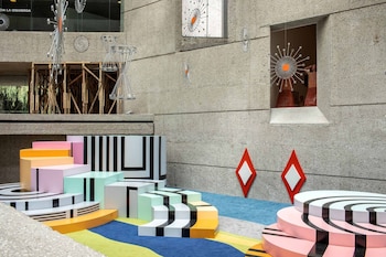 Muro de concreto y suelo multicolor. Instalación de bloques geométricos pastel y rayas negras. Adornos de estrella y rombos en paredes. Estructura de madera al fondo