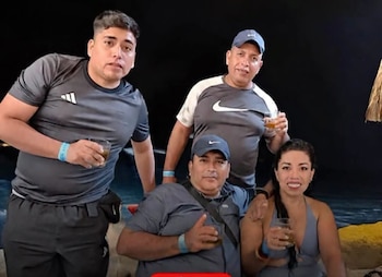 Tres hombres y una mujer vestidos con ropa deportiva sostienen vasos pequeños con bebida sobre un fondo oscuro