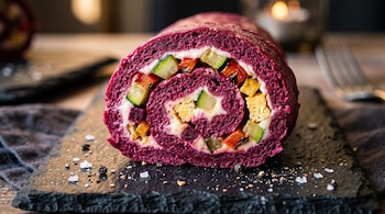 Rodaja de roll morado relleno de queso blanco, zucchini y morrón en cubos sobre una tabla de pizarra con sal.