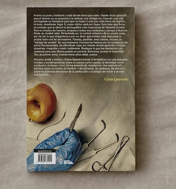 Contraportada de un libro con texto sobre identidad, una mano enguantada azul sostiene un bisturí, junto a instrumentos quirúrgicos y la mitad de un durazno