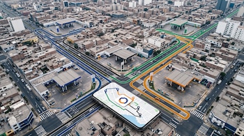 Vista aérea de calles con estaciones de servicio, líneas de colores sobre las vías y un teléfono móvil con un mapa en pantalla.