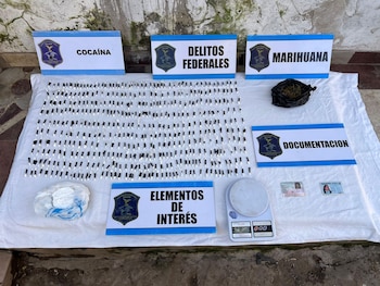 Dosis de sustancia blanca, una balanza digital, documentos y carteles indicativos expuestos sobre una sábana blanca