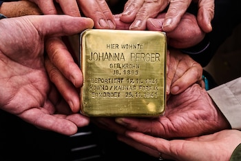 Primer plano de varias manos sosteniendo una placa de latón cuadrada, un Stolperstein, con la inscripción de los datos de Johanna Berger