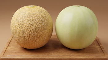 Un melón cantalupo de cáscara reticulada y un melón honeydew de piel lisa colocados sobre una tabla de madera.