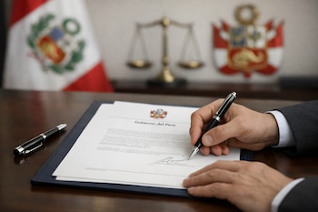 Manos firmando un documento con el membrete "Gobierno del Perú" y el escudo nacional; bolígrafo sobre una mesa, bandera peruana y balanza al fondo.