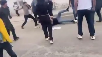Varias personas en movimiento sobre una superficie pavimentada clara, algunas corriendo y un individuo con ropa oscura en el suelo cerca de otros