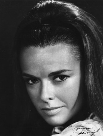 Retrato en blanco y negro de una mujer con cabello oscuro recogido hacia atrás, hombro derecho visible y una firma manuscrita en la esquina inferior derecha