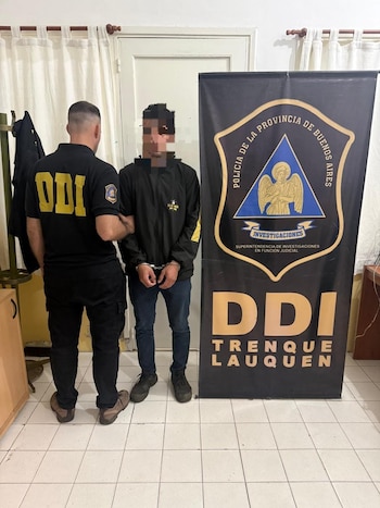 Un policía de espaldas sostiene a un hombre esposado con el rostro pixelado junto a un cartel de la DDI Trenque Lauquen
