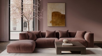 Sala moderna con sofá modular grande color malva, mesa de centro de madera oscura, pintura abstracta, ventana de piso a techo y árbol con flores rosas.