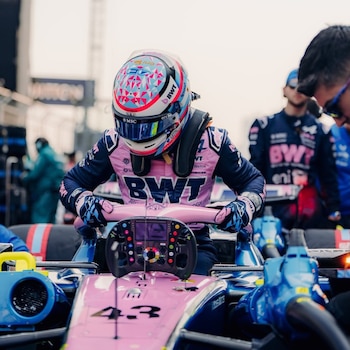 Franco Colapinto, con casco y mono de carreras rosa y azul, sentado en un coche de carreras rosa y azul con el número 43. Mira el volante