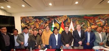 Grupo de doce hombres adultos posando en una sala de conferencias. Al fondo, un mural abstracto colorido y varias banderas nacionales