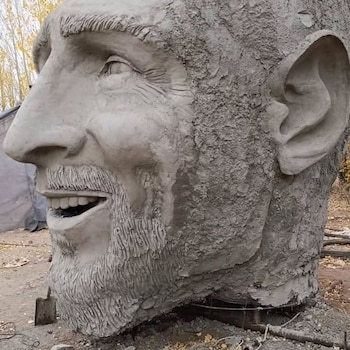 Vista de una enorme estatua de Lionel Messi vestido con la camiseta argentina, con el brazo levantado, frente a una multitud de personas con banderas