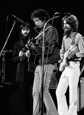 En blanco y negro, Ringo Starr con maracas, Bob Dylan con guitarra y armónica, y George Harrison con guitarra eléctrica en el escenario
