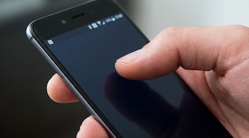 Primerísimo plano de una mano sosteniendo un teléfono móvil negro, con el ícono de NFC claramente visible en la esquina superior izquierda de la pantalla oscura.