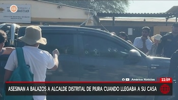 Una camioneta SUV oscura con el vidrio de la ventanilla del lado del pasajero perforado por múltiples impactos de bala, con personas observando alrededor