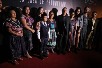 Once personas, cinco hombres, cinco mujeres y un niño, posan en una alfombra roja. Algunas mujeres llevan atuendos tradicionales con tejidos coloridos