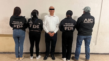 Un hombre esposado entre cuatro personas que visten chaquetas negras con logos de Policía de Investigación PDI y AIC Morelos.