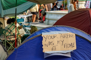 Cartel de cartón pegado en una tienda de campaña azul con el texto escrito a mano en inglés YOUR AIRBNB WAS MY HOME