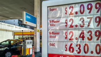 Tablero de precios de combustibles en una estación Shell, mostrando los valores de Super, V-Power Nafta, V-Power Diesel y GNC, junto a un taxi negro y amarillo en el surtidor