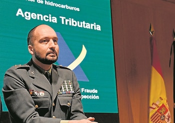 Antonio Balas en uniforme militar frente a una pantalla de la Agencia Tributaria y la bandera de España