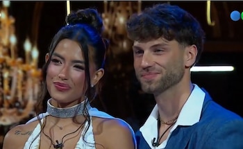 Primer plano de una mujer y un hombre jóvenes. Ella viste vestido blanco, collar brillante y aretes. Él lleva traje azul y camisa blanca