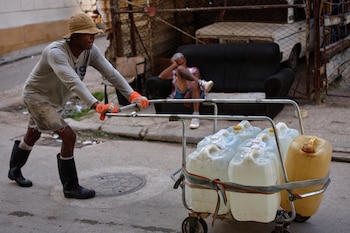 Un hombre empuja un carrito lleno de bidones de agua mientras otro descansa en un sofá en una calle de La Habana, Cuba, el jueves 27 de agosto de 2026. (Infobae Centroamérica/ AP/Ramón Espinosa)