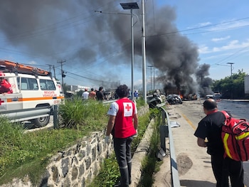 Varios socorristas con uniformes blancos y rojos inspeccionan un automóvil negro destruido junto a la estructura de un camión