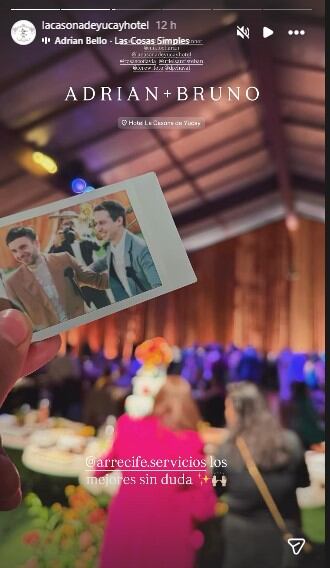 Una mano sostiene una fotografía instantánea de Bruno Ascenzo y Adrián Bello sonriendo en su boda, con el ambiente festivo de la recepción de fondo en Cusco.