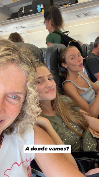 Tres mujeres sentadas dentro de un avión; se observa a una mujer de cabello rubio rizado, una mujer de cabello castaño y otra de cabello rubio recogido