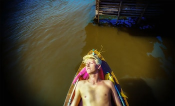 David Bowie yace con los ojos cerrados y el torso descubierto en una embarcación de madera sobre agua de tono moscado