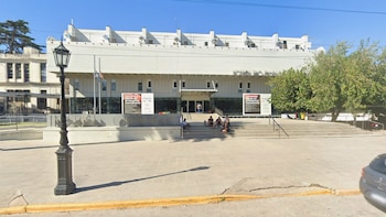 Fachada del Hospital Centenario con personas sentadas en las escalinatas de acceso y un farol sobre la vereda