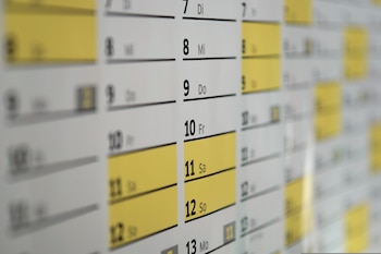 Primer plano de un calendario o planificador semanal en papel, con filas de días y números. Los días 11 y 12 están resaltados con barras amarillas