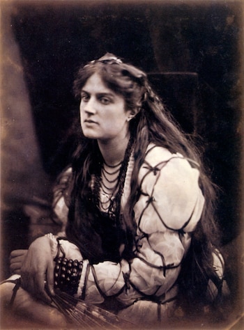 Retrato en sepia de una mujer de cabello largo y oscuro, con una blusa clara y collares, sosteniendo objetos finos en su mano, mirando al costado